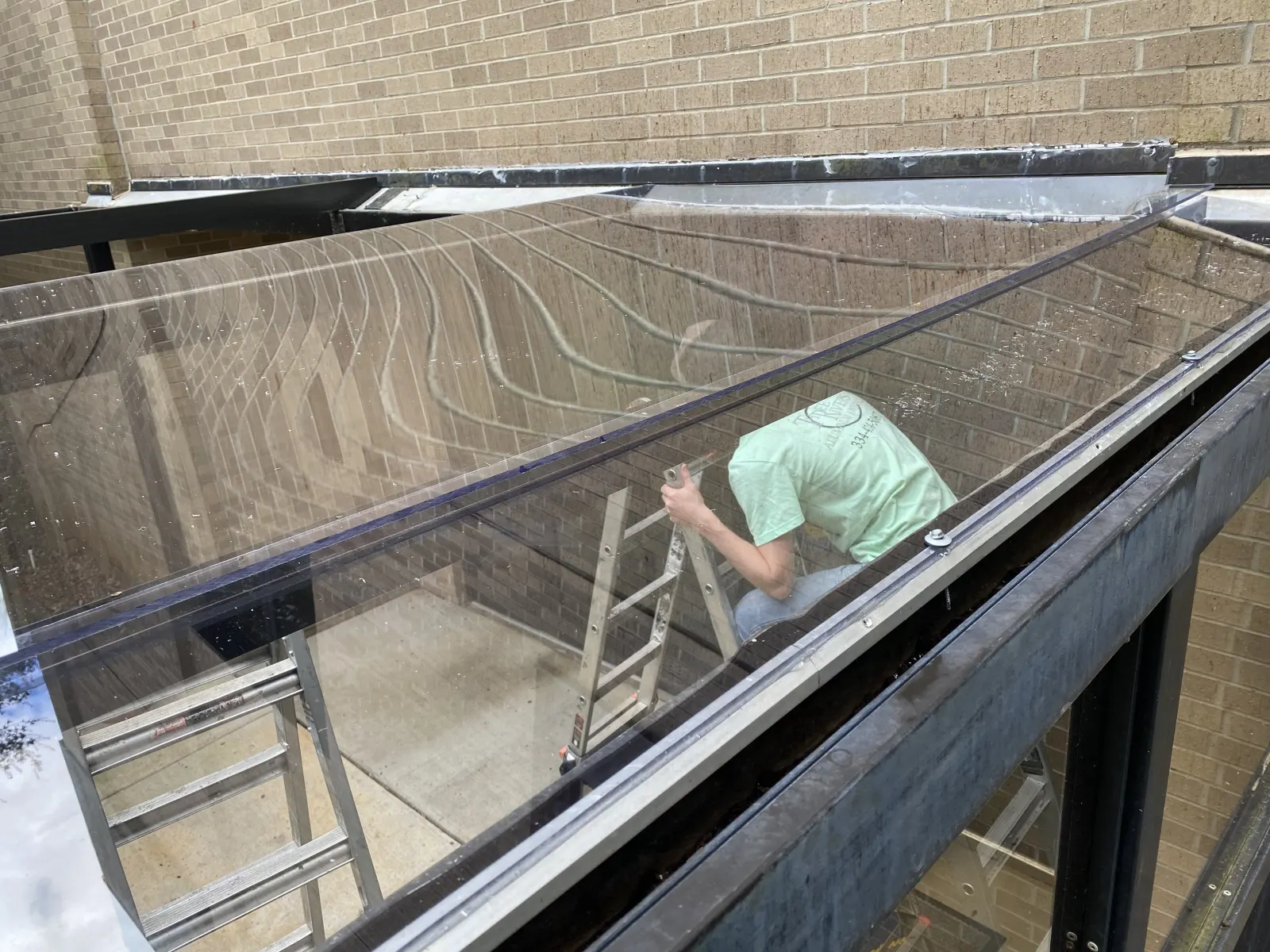 Installer fitting clear roof panels on an aluminum canopy between two buildings
